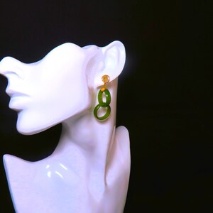 May include: A pair of green jade earrings with gold accents. The earrings are in the shape of two interlocking circles.