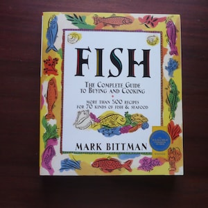 May include: A cookbook titled "FISH" with a colorful cover featuring illustrations of various fish and seafood. The book is a complete guide to buying and cooking, with over 500 recipes for 70 kinds of fish and seafood. The author's name, Mark Bittman, is also visible.
