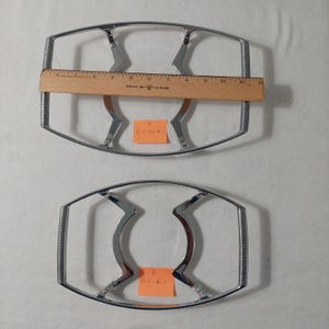 May include: Two silver metal cake cooling racks, one larger than the other, on a white surface. The larger rack is labeled "A P-11-23-K-1" and the smaller rack is labeled "B P-11-23-K-1".