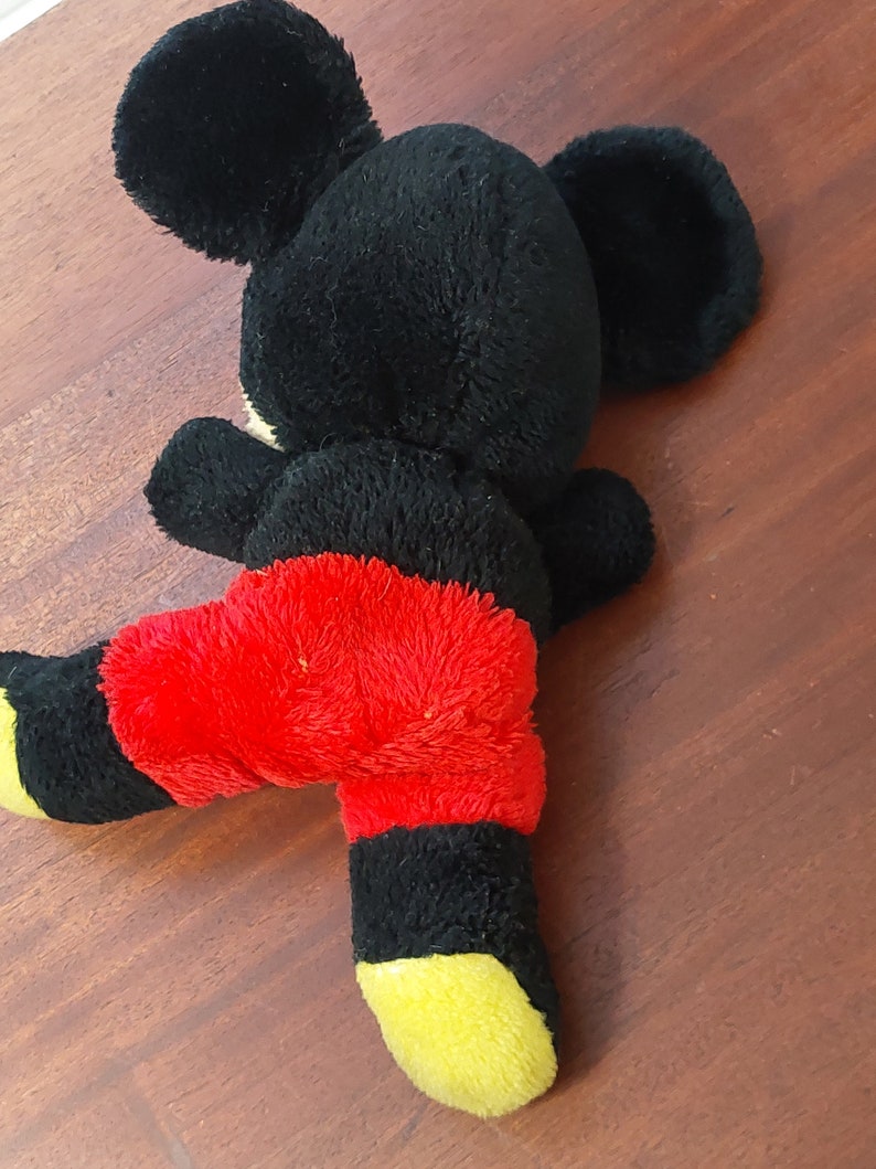May include: Black and red plush Mickey Mouse toy with yellow accents. The toy is lying on its back with its legs in the air.