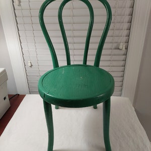 May include: A green wooden chair with a rounded seat and curved legs. The chair has a simple design with a slightly distressed finish.