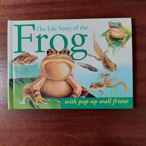May include: A children's book titled "The Life Story of the Frog" with a pop-up wall frieze. The cover features illustrations of frogs in different stages of life, including tadpoles, a froglet, and an adult frog.
