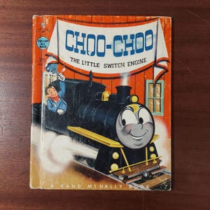 May include: Vintage children's book cover featuring a smiling cartoon train. The title "CHOO-CHOO The Little Switch Engine" is displayed above the train illustration. The cover has an orange and white banner design with a small illustration of a boy.