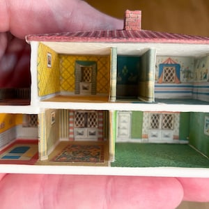 May include: A miniature two-storey dollhouse structure featuring an open-front design with multiple rooms. The interior walls display colourful patterned wallpaper in yellow, green, and blue, while the exterior roof is a textured reddish-brown.