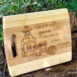 May include: A wooden cutting board with a laser-engraved design featuring a bottle of tequila, two shot glasses, a lime wedge, and the text "Take Life with a Grain of salt A Slice of lime & A SHOT of Tequila".