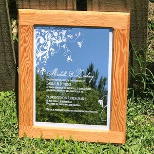 May include: A wooden framed mirror with a white floral design and the text "Michelle & Zachary"  "REQUEST THE PLEASURE OF THE COMPANY OF" "BARRY & JUSTINE" "AT THEIR MARRIAGE ON SATURDAY, 21 JANUARY 2017" "A GARDEN CEREMONY WILL TAKE PLACE AT" "FLORENTINO'S RESTAURANT" "18 BAY STREET, SOMMERVILLE" "FOLLOWED BY FINE FOOD AND DANCING" "WE LOOK FORWARD TO SHARING THIS SPECIAL DAY WITH YOU"