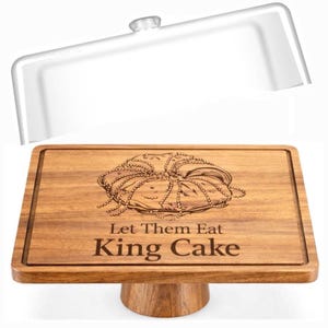 May include: Wooden cake stand with a clear plastic lid. The rectangular stand features a carved design of a King Cake and the words "Let Them Eat King Cake". The stand is supported by a round wooden base. A perfect addition for serving desserts.