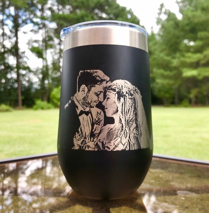 May include: Black stainless steel tumbler with a laser engraved image of a couple in a wedding setting. The image is in silver.