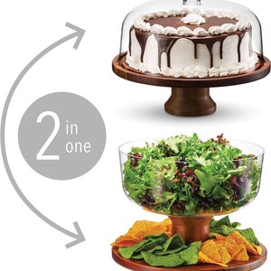 May include: A two-in-one wooden serving stand with a glass dome for cakes and a glass bowl for salads. The stand has a brown wooden base and a round wooden top. The glass dome is clear and has a knob on top. The glass bowl is clear and has a wide rim. The stand is shown with a chocolate cake under the dome and a salad in the bowl.