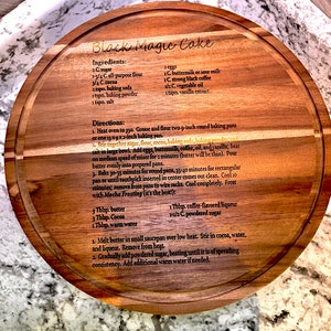 May include: A wooden cutting board with a recipe for Black Magic Cake engraved on it. The recipe includes ingredients like sugar, flour, cocoa, baking soda, baking powder, salt, eggs, buttermilk, coffee, oil, and vanilla. The recipe also includes instructions for baking the cake and making a mocha frosting.