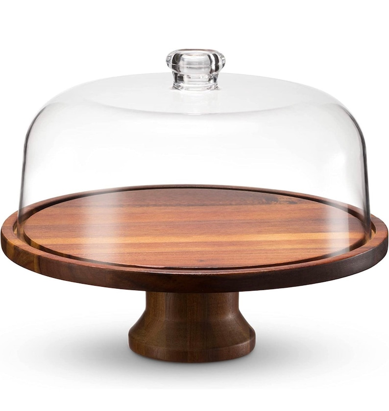 May include: A wooden cake stand with a clear glass dome. The stand has a round base and a pedestal.