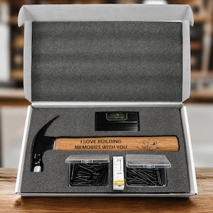 May include: A hammer, level, tape measure, and nails are displayed in a gift box. The hammer has a wooden handle with the text "I LOVE BUILDING MEMORIES WITH YOU". The box is open, revealing the tools.