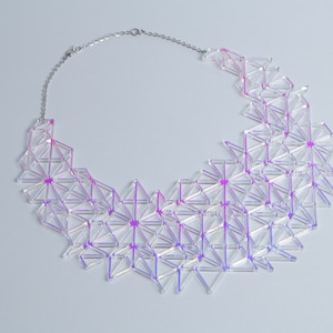 May include: A geometric statement necklace featuring a clear, iridescent design with pink and purple accents. The necklace is composed of interconnected triangular shapes and is suspended from a silver chain.