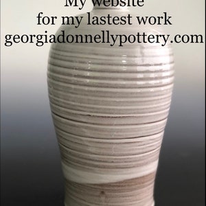 Könnte beinhalten: Weiße Keramikvase mit einem gestreiften Muster. Die Vase ist hoch und schlank mit einem abgerundeten Boden. Bitte besuchen Sie georgiadonnellypottery.com für weitere Informationen.
