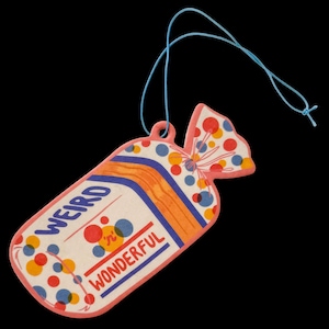 May include: A whimsical, pink-edged air freshener shaped like a candy wrapper, with the words "WEIRD 'n' WONDERFUL" printed on it. The design features colorful polka dots and orange and blue stripes. A blue string is attached for hanging.