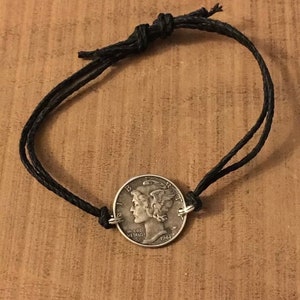 May include: A black cord bracelet with a silver 1944 United States Mercury dime coin charm.