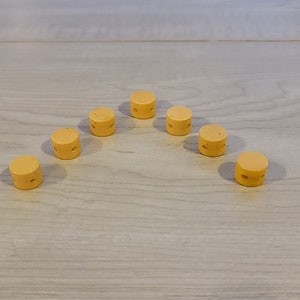 May include: Seven small, round, yellow wooden knobs with holes in the center. The knobs are arranged in a semi-circle shape.