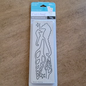 May include: A Cuttlebug die set with sea-themed designs, including seahorses, seashells, and starfish. The package includes two dies and is made by Provo Craft. The die set is in a clear plastic package.