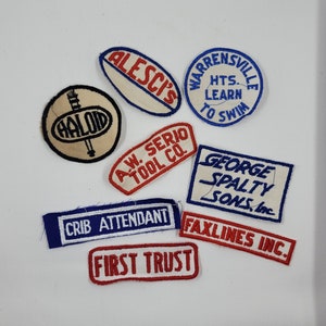 May include: A collection of nine vintage embroidered patches. The patches are various shapes and sizes and feature different colors, including red, blue, white, and black. The patches feature text, including "Haloid", "Alesci's", "A.W. Serio Tool Co.", "Warrenville Hts. Learn to Swim", "George Spalty Sons, Inc.", "Faxlines Inc.", "First Trust", and "Crib Attendant".