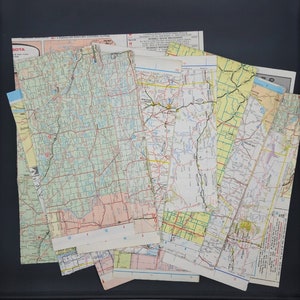 May include: A collection of vintage paper maps of the United States, featuring a variety of states and regions. The maps are in various shades of green, blue, and yellow, with black lines indicating roads and highways. The maps are slightly worn and faded, giving them a vintage look.