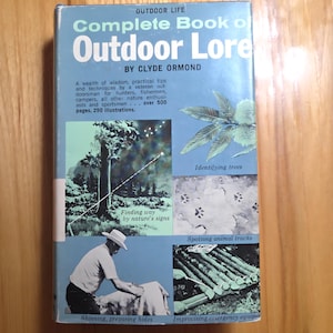 May include: A vintage book titled "Complete Book of Outdoor Lore" by Clyde Ormond. The cover is light blue with white and black text and illustrations about nature, including tree identification and animal tracks.