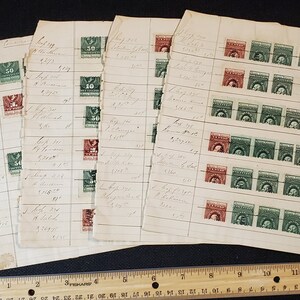 May include: A collection of vintage stamps on a sheet of paper with handwritten notes. The stamps are green and red with images of a man's profile. The paper is yellowed and has a ruler next to it.