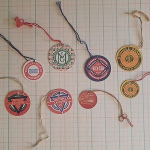 May include: A collection of eight vintage round and triangular paper tags with string attached. The tags feature various logos and text, including "Wright & Nelmy Co. Hardware", "Dutton Lainson Co.", "Superior Quality Rich-Con", "Midhawk Brand The Brand of Quality", and "Since 1882 Dutton Lainson Co."