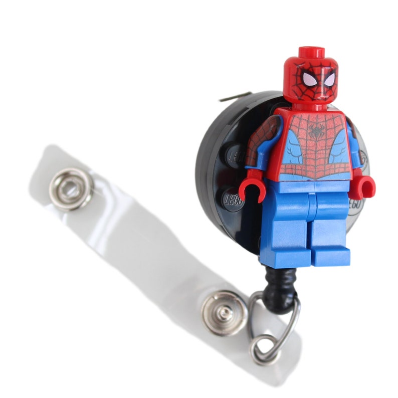 May include: A red and blue Lego minifigure of Spider-Man attached to a black retractable badge reel. The reel has a clear plastic badge holder with a metal clip.