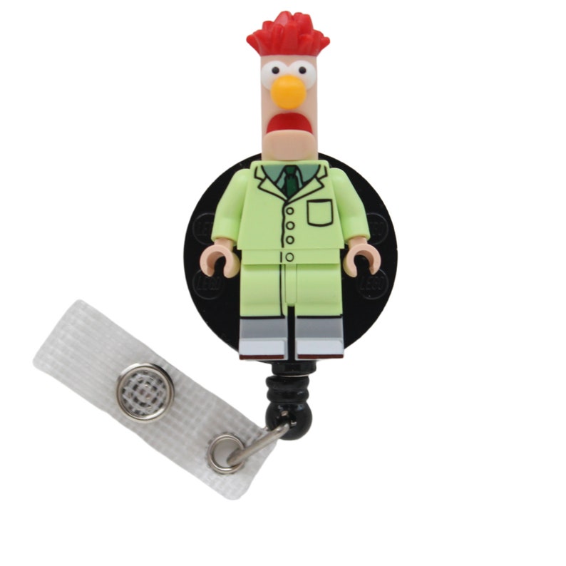 May include: A green and red Lego minifigure of a rooster wearing a lab coat and a green tie. The minifigure is attached to a black retractable badge holder with a white strap.