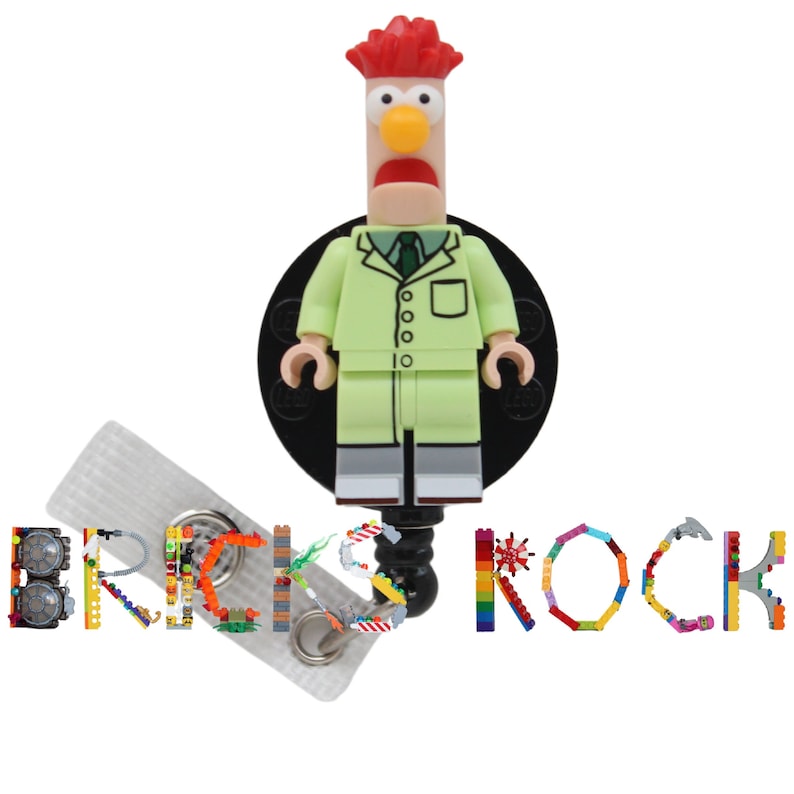 May include: A green and white Lego minifigure of a red-haired character wearing a lab coat and a green tie. The minifigure is attached to a black retractable badge holder with a clear plastic strap. The word "BRICKS ROCK" is spelled out in Lego bricks below the minifigure.