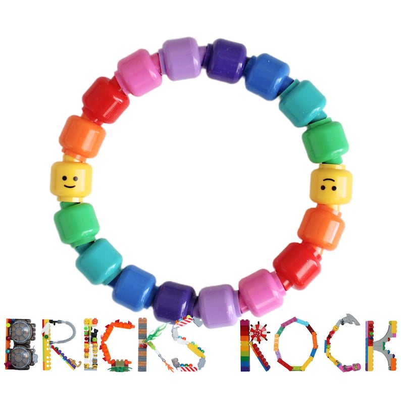 Op de afbeelding: Een kleurrijke armband gemaakt van Lego-achtige blokken in een regenboog van kleuren. De armband bevat twee gele blokken met lachende gezichten. Het woord "BRICKS ROCK" is eronder in Lego-blokken geschreven.
