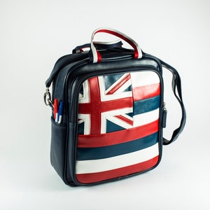 May include: A navy blue shoulder bag with a Union Jack design in red, white, and blue. The bag has a top handle with red and white stripes, a side pocket with pens, and a detachable shoulder strap.