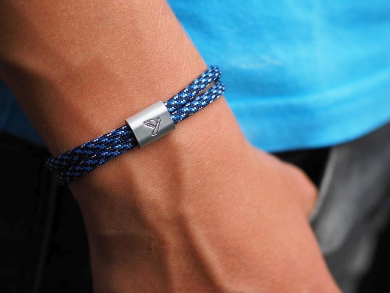 Seilarmband mit Element aus Aluminium mit Schutzengelprägung. Bandfarbe verschiedene Blautöne.Armband ist durch spezielle Knoten in der Größe verstellbar.
