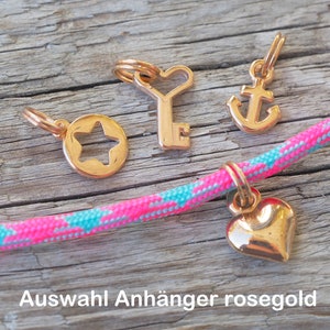 Op de afbeelding: Vier rozen gouden bedels: een ster, een sleutel met een hart, een anker en een hart. De bedels zijn op een roze en turquoise touw.