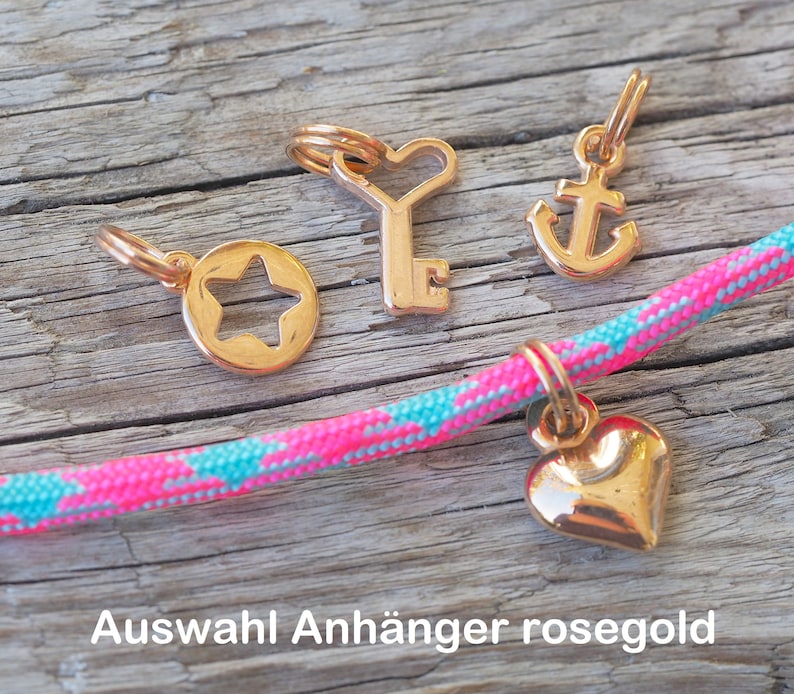 Op de afbeelding: Vier rozen gouden bedels: een ster, een sleutel met een hart, een anker en een hart. De bedels zijn op een roze en turquoise touw.