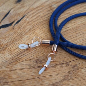 Op de afbeelding: Een paar brillenhouders in marineblauw met ros&eacute;gouden metalen accenten en transparante kunststof tips.
