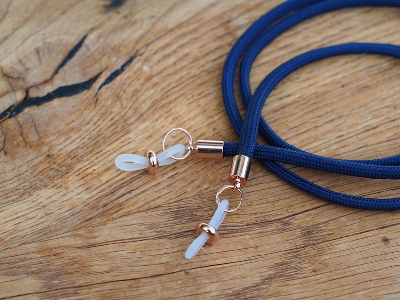 Op de afbeelding: Een paar brillenhouders in marineblauw met ros&eacute;gouden metalen accenten en transparante kunststof tips.