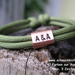Könnte beinhalten: Ein grünes Paracord-Armband mit einem kupfernen Metalletikett, das mit den Initialen "A&A" graviert ist.