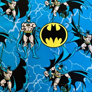 May include: A blue fabric with a repeating pattern of Batman in a black suit with a yellow bat symbol on his chest. The background is a blue and white lightning bolt pattern.