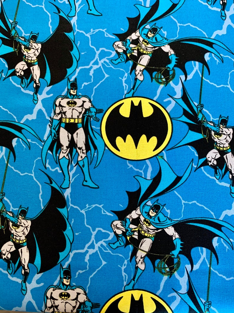 May include: A blue fabric with a repeating pattern of Batman in a black suit with a yellow bat symbol on his chest. The background is a blue and white lightning bolt pattern.