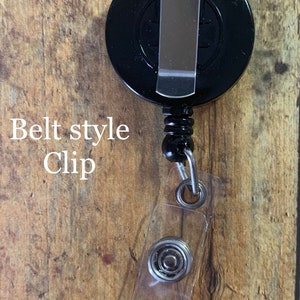 May include: A black retractable badge reel with a belt-style clip. The reel has a clear plastic snap closure for attaching to a badge or ID. The text "Belt style Clip" is visible.