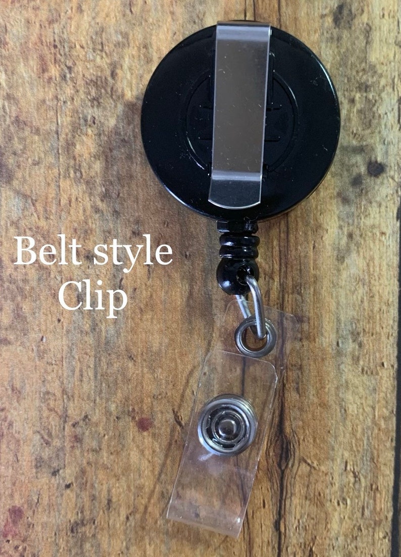 May include: A black retractable badge reel with a belt-style clip. The reel has a clear plastic snap closure for attaching to a badge or ID. The text "Belt style Clip" is visible.