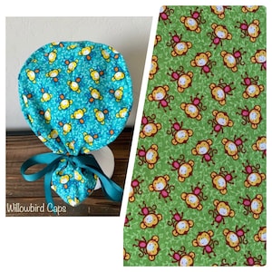May include: A turquoise blue surgical scrub cap with a monkey pattern. The cap has a tie at the back and a small pouch on the front. The fabric is printed with yellow monkeys on a green background.