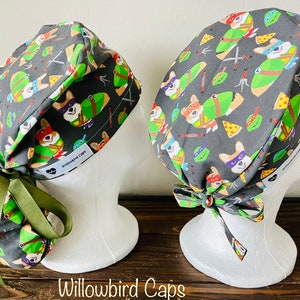 May include: Two grey surgical caps with a green, red, and blue print of corgis dressed as Teenage Mutant Ninja Turtles. The caps have green ties and the text "Willowbird Caps" is printed on the side.