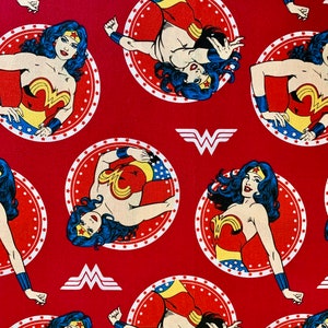 May include: Red fabric with a repeating pattern of Wonder Woman in a red, blue and gold costume. She is standing in a circle with stars and the Wonder Woman logo.