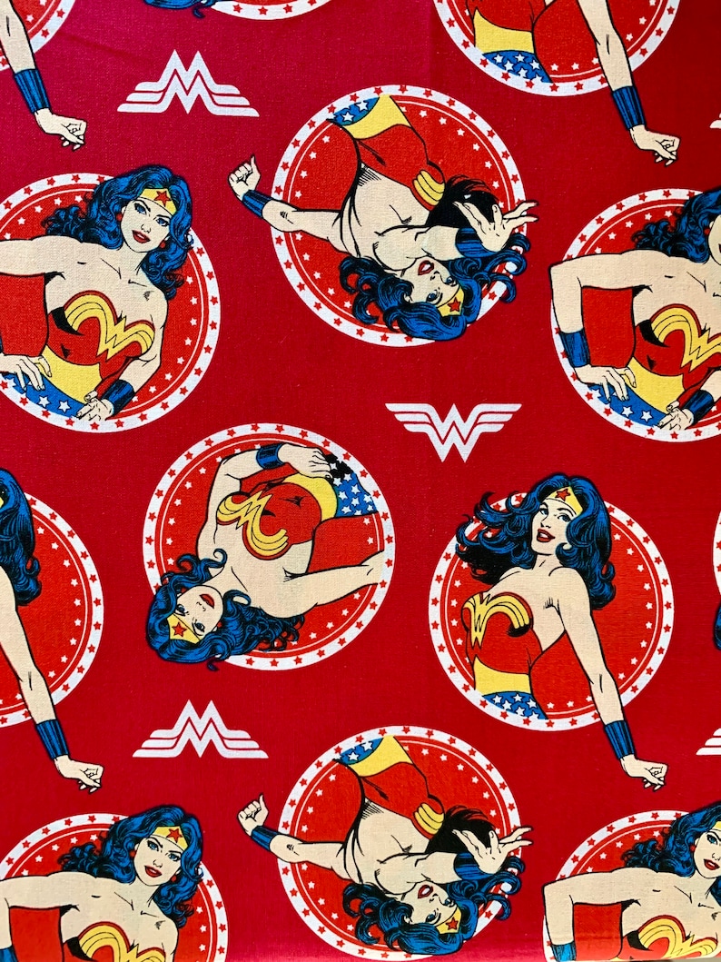 May include: Red fabric with a repeating pattern of Wonder Woman in a red, blue and gold costume. She is standing in a circle with stars and the Wonder Woman logo.