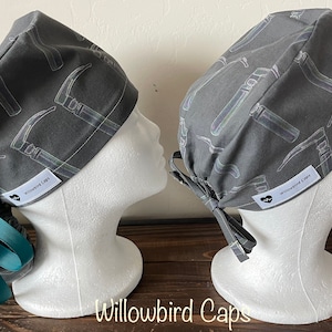 Może przedstawiać: Dwa szare czepki chirurgiczne z białym wzorem młotka i białą etykietą z napisem "Willowbird Caps".