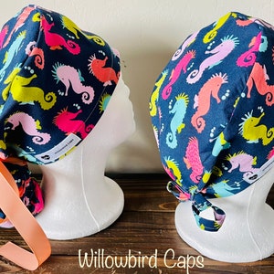 May include: Two blue surgical caps with a colorful seahorse pattern. The caps have a tie at the back and are made by Willowbird Caps.