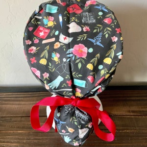 May include: A black scrub hat with a colorful floral and medical themed print. The hat has a red ribbon tied around it. The text "Willowbird Caps" is visible at the bottom of the image.