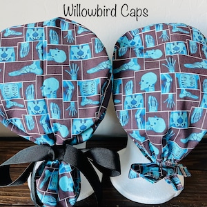 May include: Two surgical caps with a blue and brown pattern of x-ray images of bones. The text "Willowbird Caps" is printed on the top of the image.